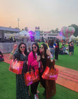 Three women posing with colorful bags at an outdoor event with a hot air balloon in the background.